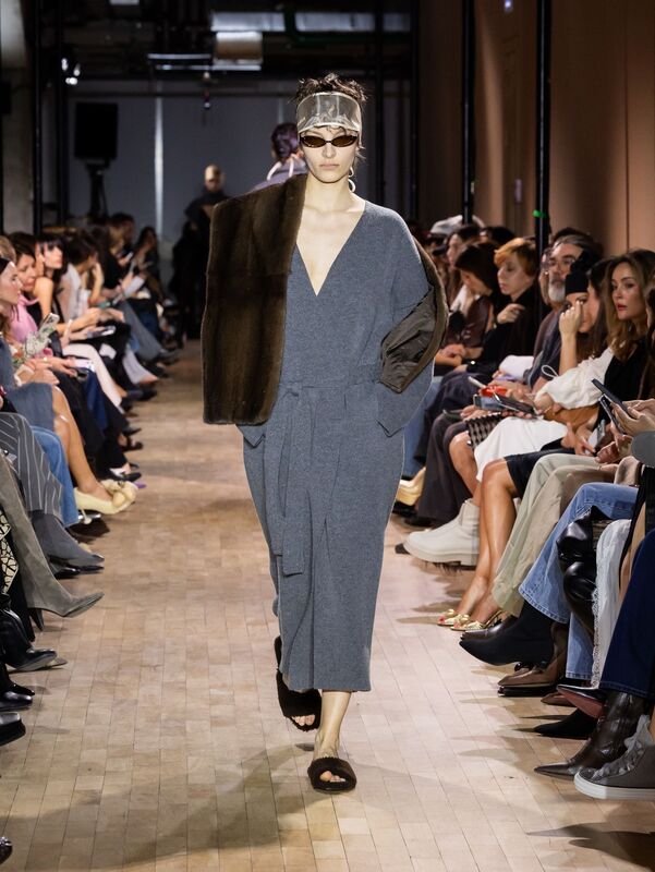 Модель в сером трикотажном наряде с глубоким вырезом и меховым палантином, завершает образ сандалиями на плоской подошве