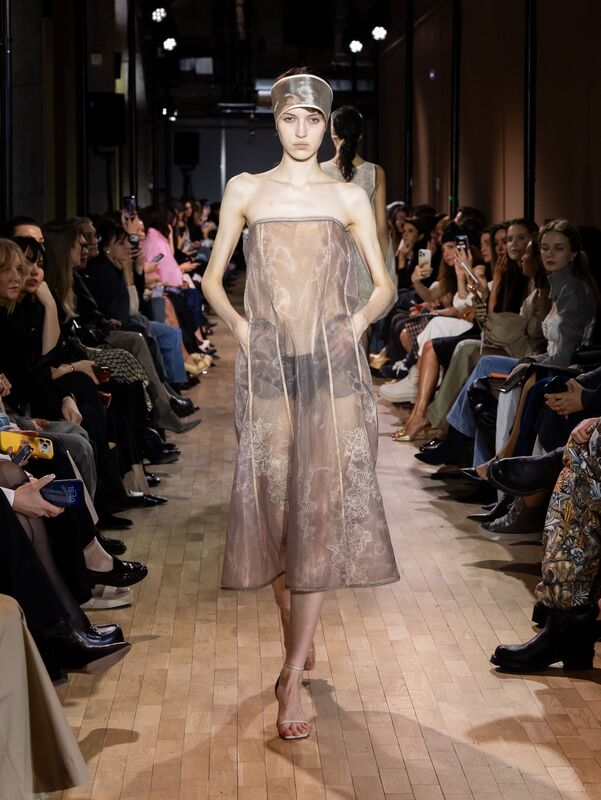 Нежное полупрозрачное платье в бежевых тонах, обрамляющее фигуру, создает романтичный и утонченный образ на подиуме