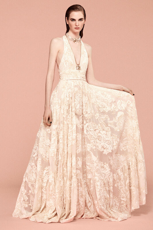 Нежное платье с глубоким вырезом и кружевной отделкой, создающее романтичный образ на фоне розового фона